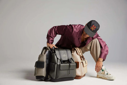 Person wearing a cap and stylish outfit, interacting with multiple backpacks in a modern studio setting.