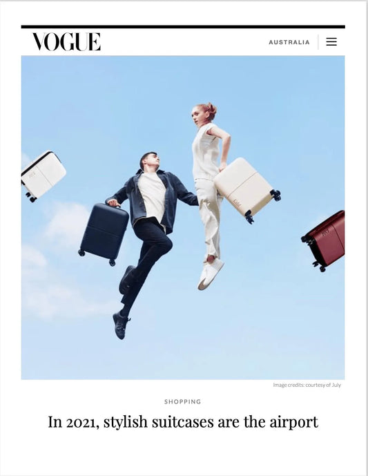 Couple in stylish outfits jumping with colorful suitcases, showcasing airport fashion in Vogue Australia.